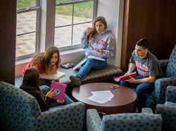 Students sitting around in a Residence Hall showing one-another things on an iPad and studying.